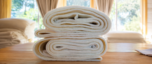 Rolled wool wadding sheets stacked on a wooden table in a warm indoor setting